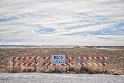 Road closed sign blocking access to a rural field under a cloudy sky.