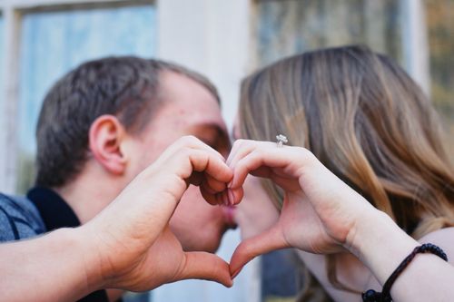 Free Close-up of a couple kissing behind a heart-shaped hand gesture, symbolizing love and connection. Stock Photo