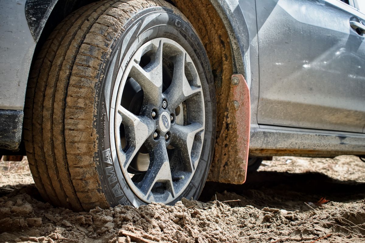 Close-up of a dusty SUV tire and wheel parked on a loose dirt and gravel road after backcountry driving