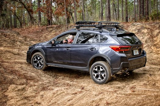 A man driving a Subaru on a rugged dirt road through a forest, showcasing off-road capabilities.