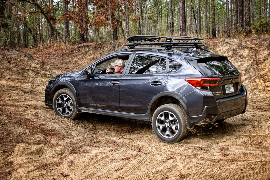A man driving a Subaru on a rugged dirt road through a forest, showcasing off-road capabilities.