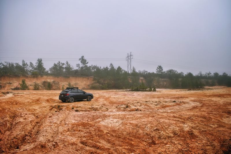 SUV driving through a foggy desert terrain with reddish soil and shrubs, capturing a sense of adventure.