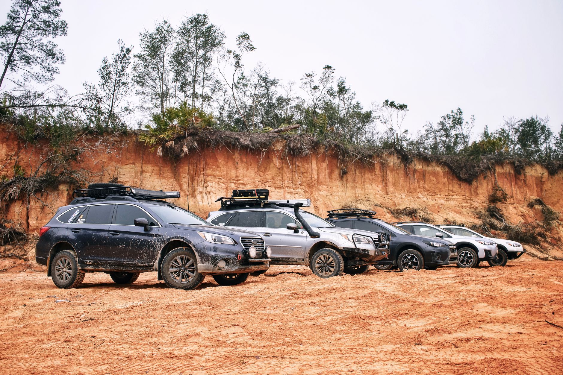 A lineup of SUVs parked on a dirt road beside a rugged terrain, ready for an off-road adventure.