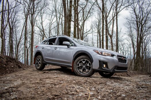 A silver SUV car driving on a rocky dirt road through a forest, showcasing off-road capabilities.