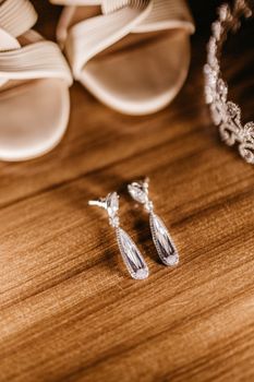 Close-up of bridal earrings, shoes, and tiara on a wooden background, exuding elegance.