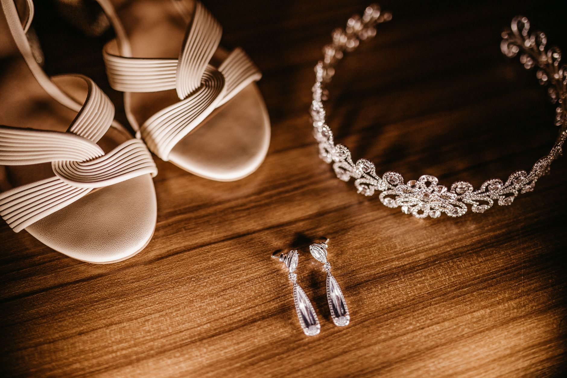 A collection of elegant bridal accessories including shoes, a tiara, and earrings on a wooden surface.