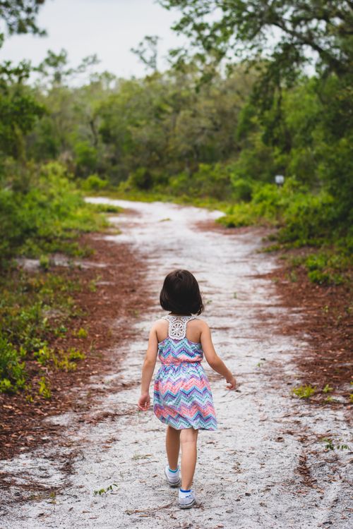 Free A child in colorful dress walks along a forest trail surrounded by greenery. Stock Photo