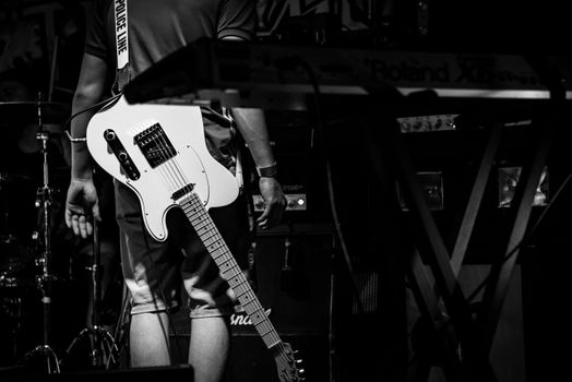 A monochrome image of a musician with a white electric guitar on stage.