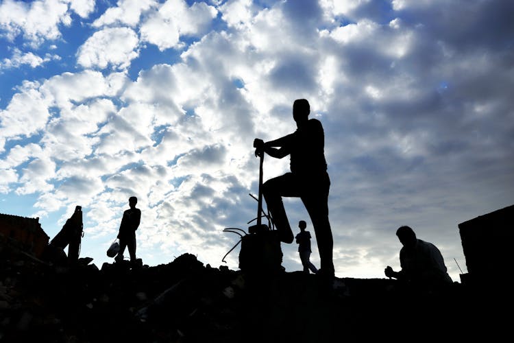 Silhouette Of Workers Under Clouds