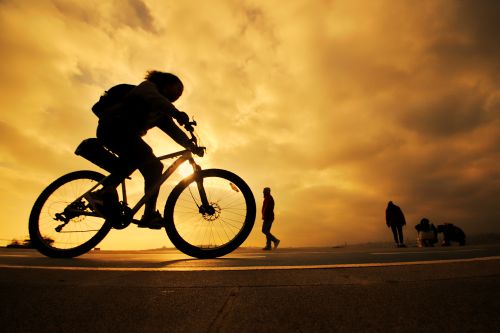 Free Silhouettes of a cyclist and pedestrians against a vibrant sunset sky, capturing motion and serenity. Stock Photo