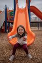 Girl in White Long Sleeve Shirt and Red Pants Sitting on Orange Slide