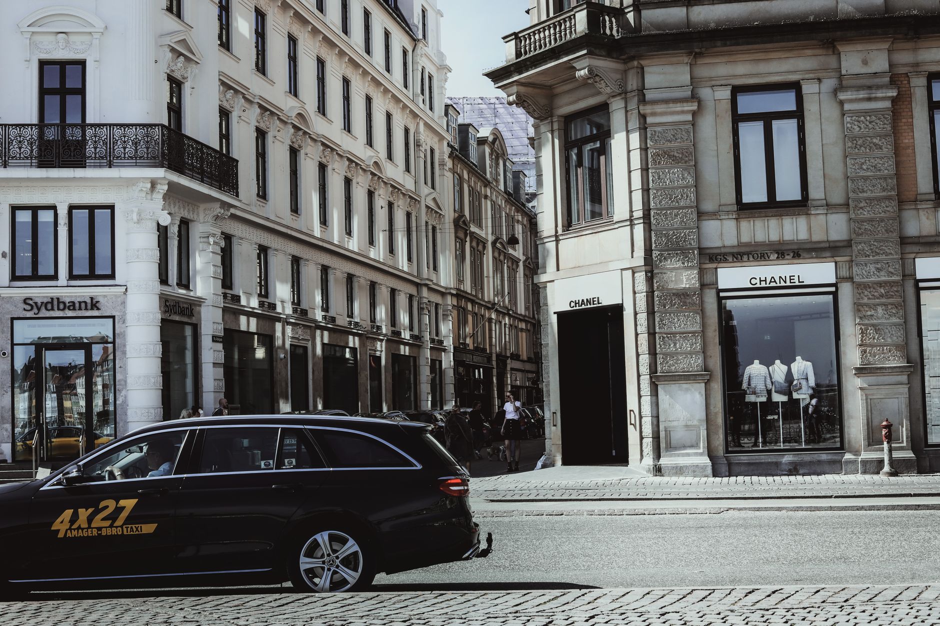 A bustling street corner in Copenhagen, featuring elegant architecture and a Chanel storefront.