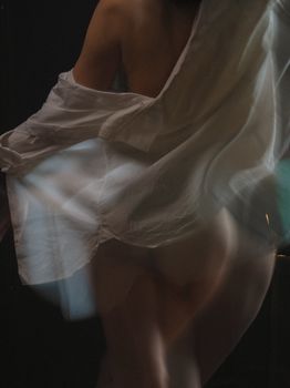 A sensual and artistic photo capturing motion blur of a woman draped in a white shirt.