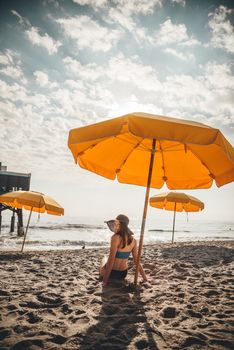 Woman relaxing under yellow umbrella on a sunny beach day.