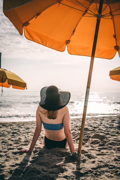 Free Woman in Bikini Sitting Under a Beach Umbrella Stock Photo
