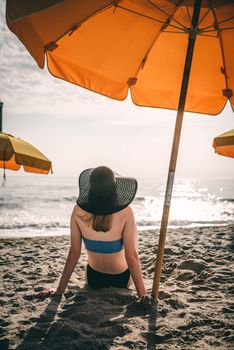 Woman sitting on the beach under vibrant umbrellas, enjoying a sunny day at the shore.