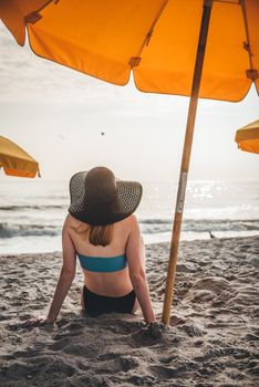 A woman in swimwear relaxes under a beach umbrella by the ocean.