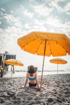 Woman sitting under yellow umbrellas on a sandy beach enjoying a sunny day.