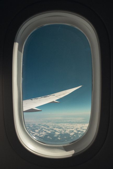 View of an airplane wing through a window, capturing a scenic sky and clouds.