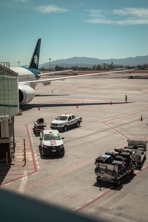 Free Airplane parked at Guadalajara airport with ground vehicles and luggage carts nearby. Stock Photo