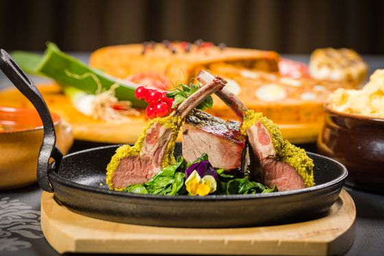 Rack of lamb chops with green herb crust on a sizzling skillet with greens and currants
