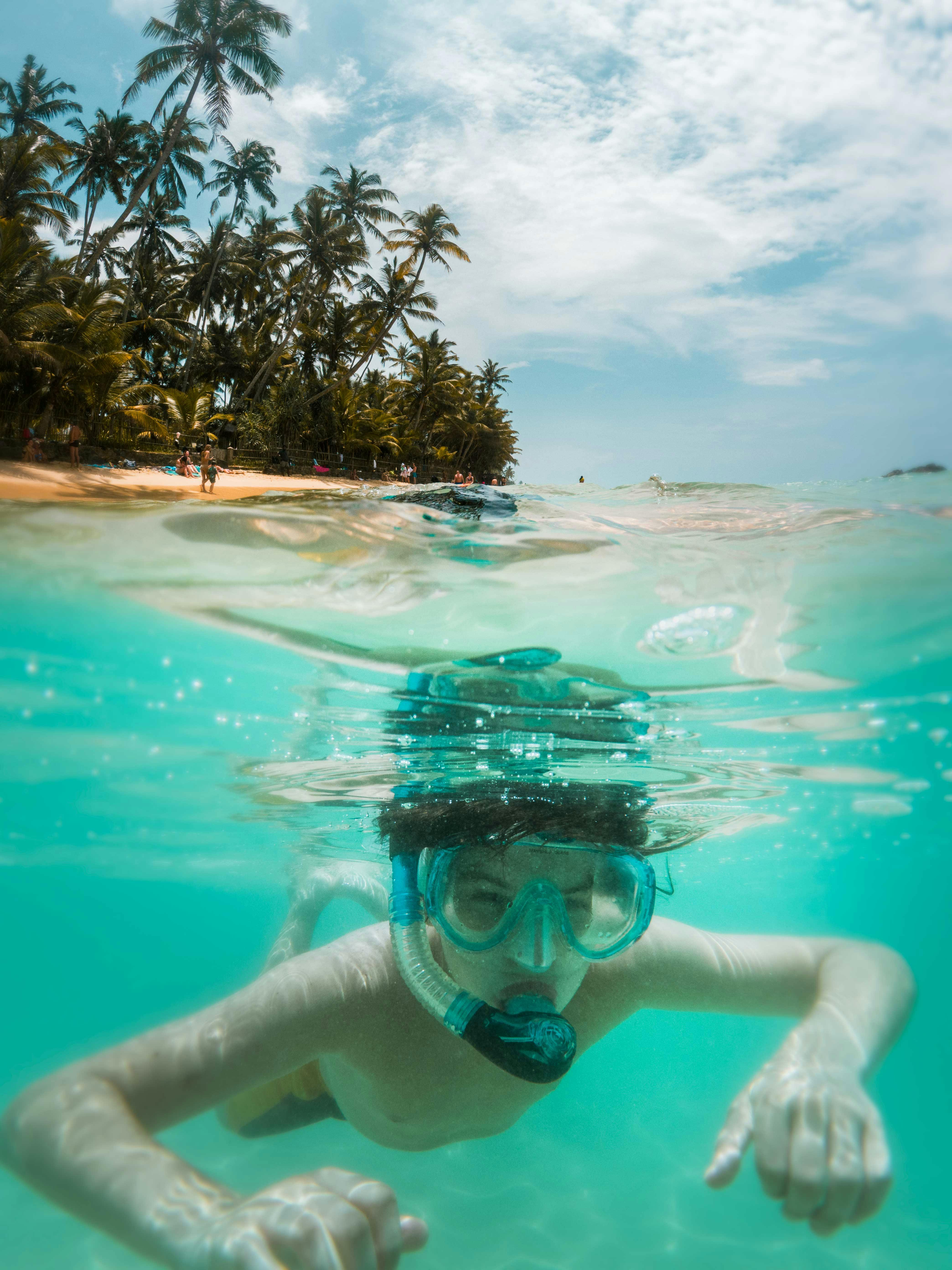 A young boy snorkeling in clear turquoise water near a tropical beach with palm trees.