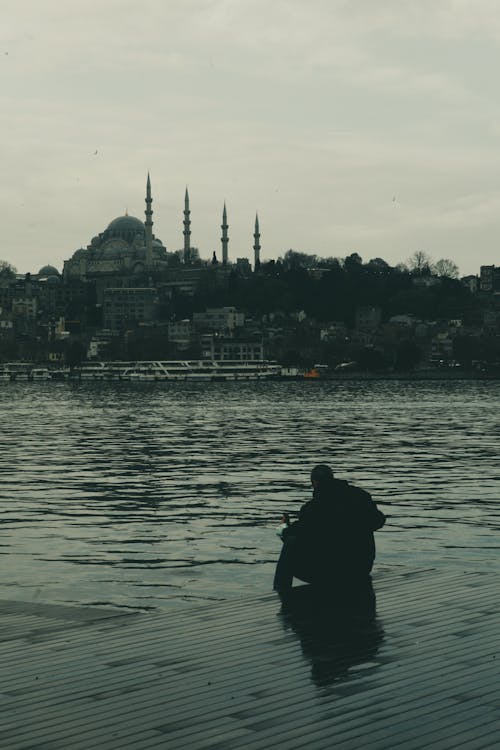 Silhouette of Man Sitting on Pier near Water