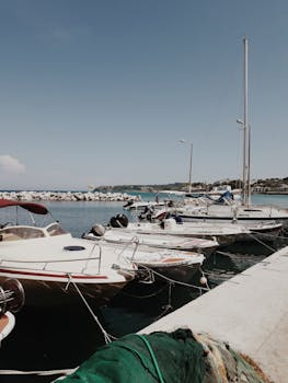 A peaceful scene of boats docked at a marina in Planos, Greece with a clear sky.