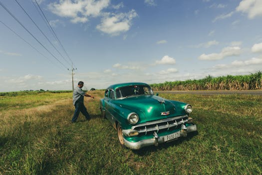 A man standing beside a classic vintage car in a rural countryside. Bright day with blue skies.
