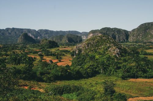 Free A vibrant landscape with green fields and majestic mountains under a clear sky. Stock Photo