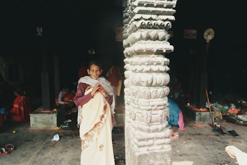Old Woman in Traditional Clothes near Column in Temple