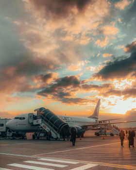 Passengers boarding an airplane at a Turkish airport during a vibrant sunset.