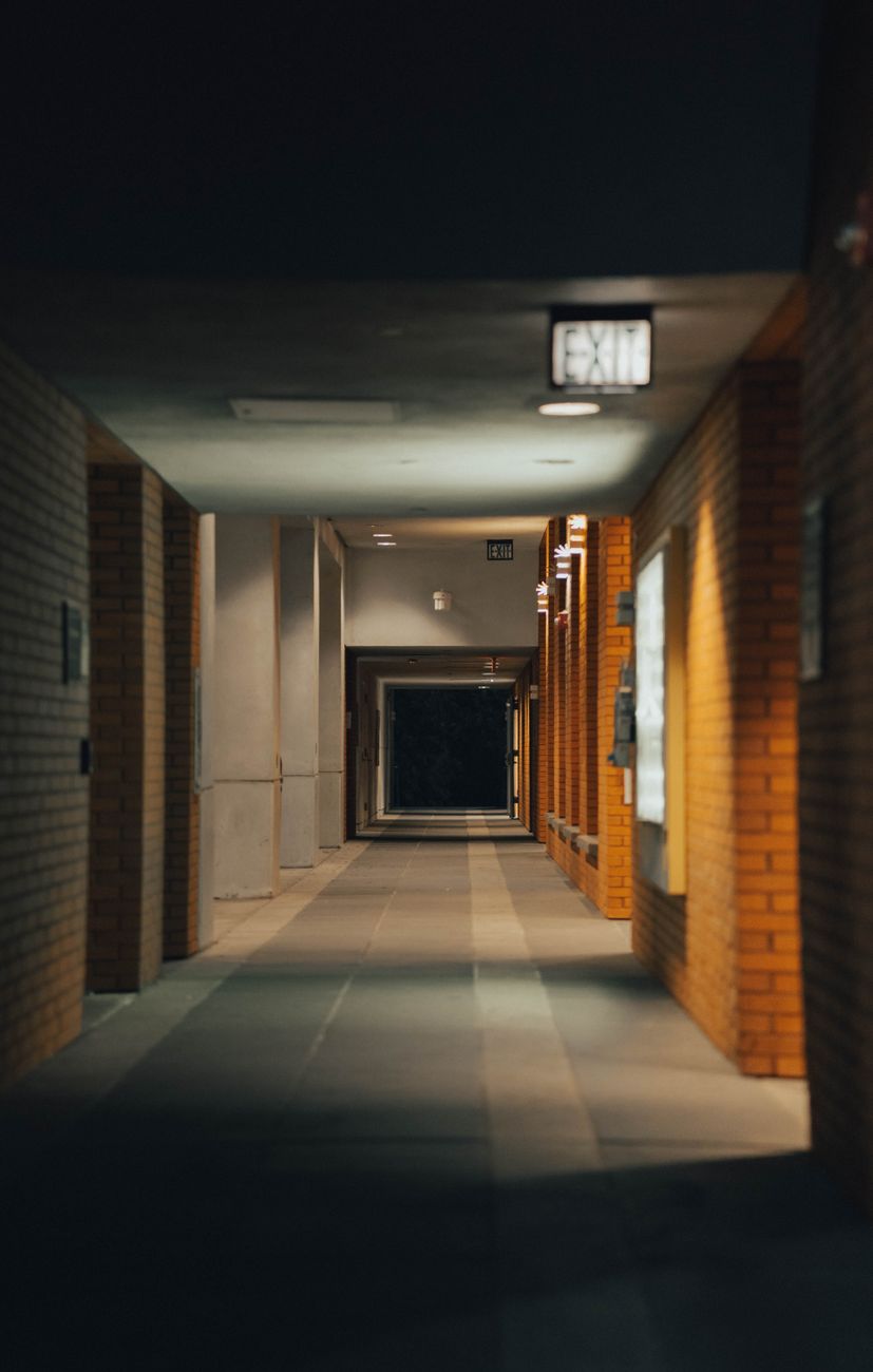 A moody, empty hallway with brick walls and overhead lights casting shadows.. moody, empty, hallway
