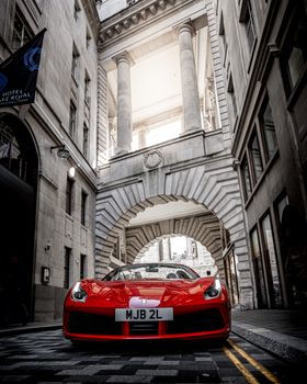 A striking red sports car parked in a historic London alleyway under the classic architecture.