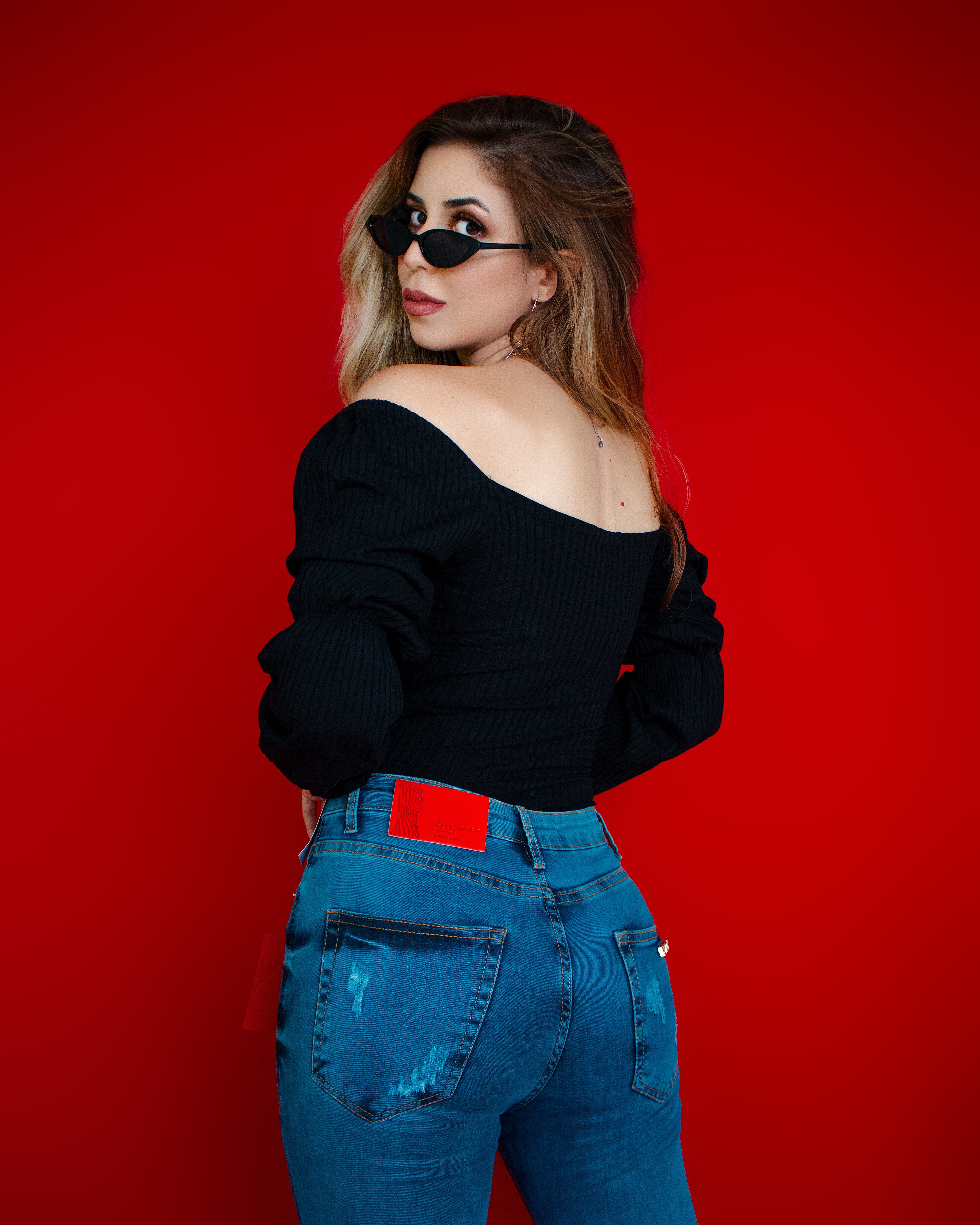 Fashion portrait of a young woman in sunglasses and black top with red background.