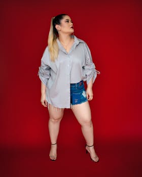 Caucasian woman in denim shorts and gray top poses confidently indoors.