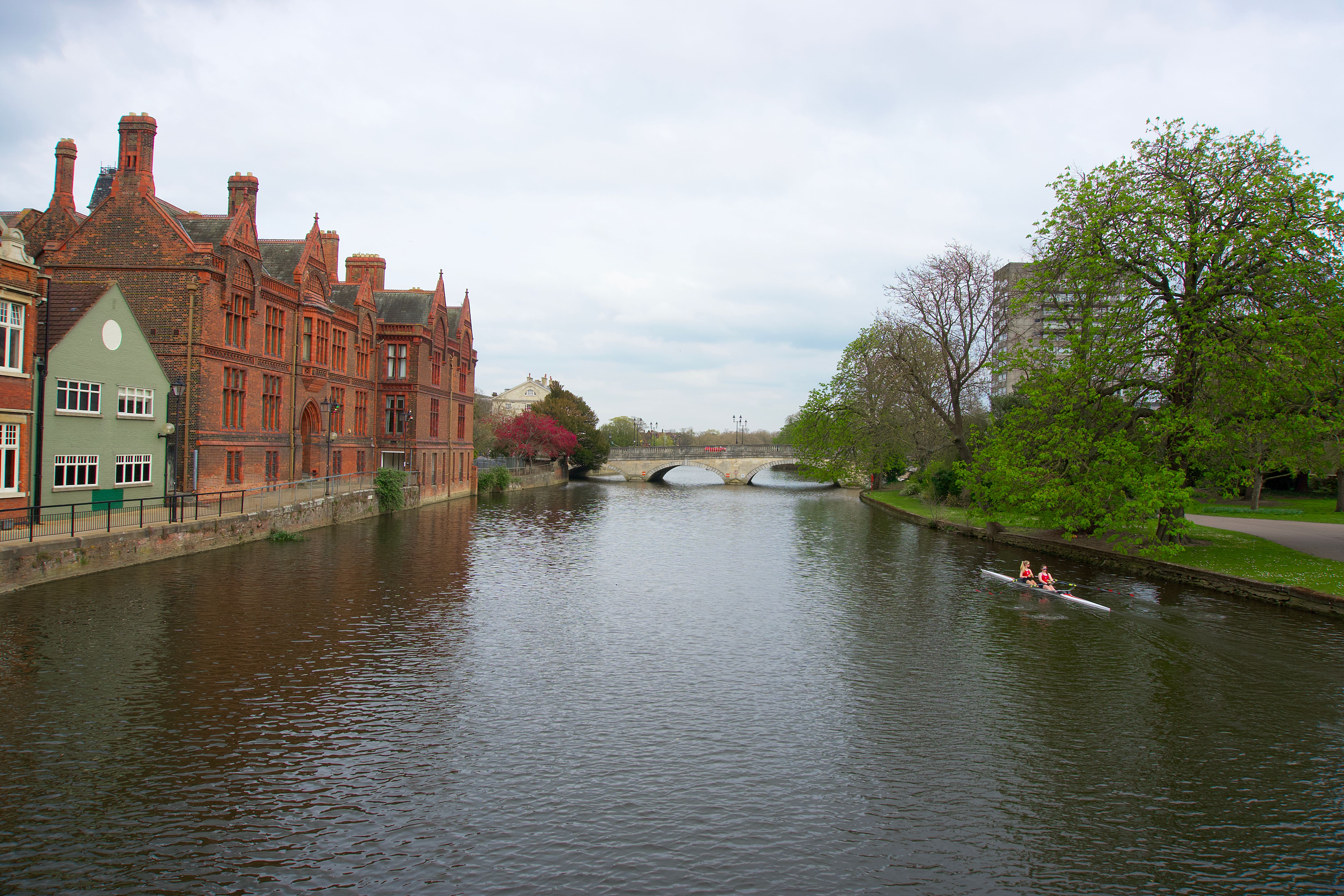Rowers on the River Great Ouse with historic brick buildings and a bridge in Bedford, England.