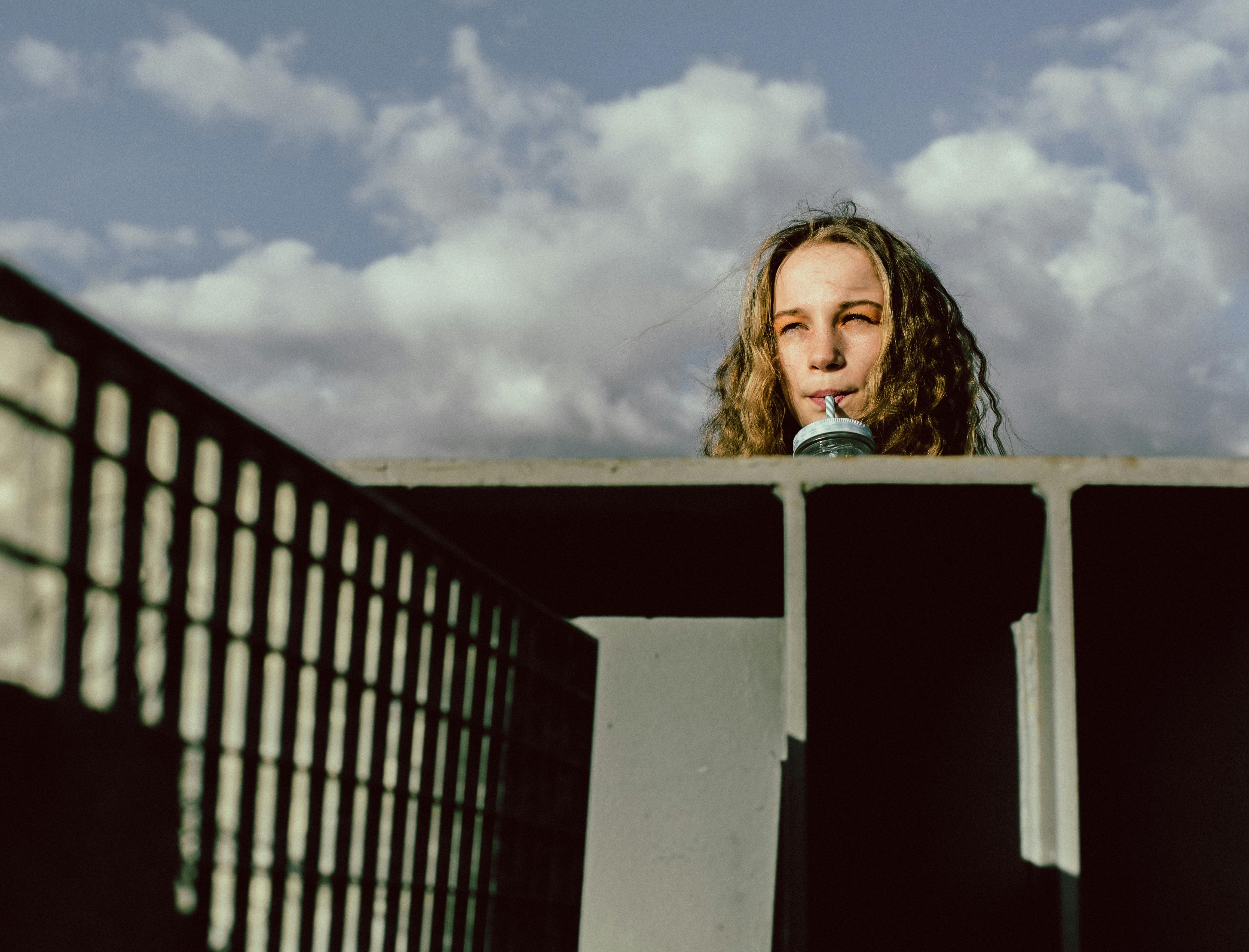 A woman sips from a straw with a moody sky background, adding a dramatic touch.