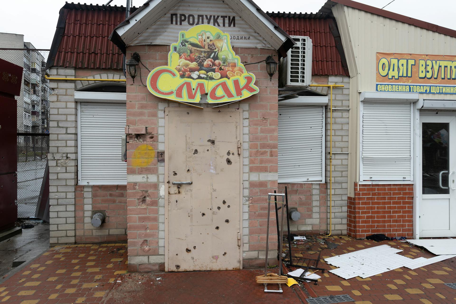 An abandoned grocery store exterior with damaged signage and debris on the pavement.