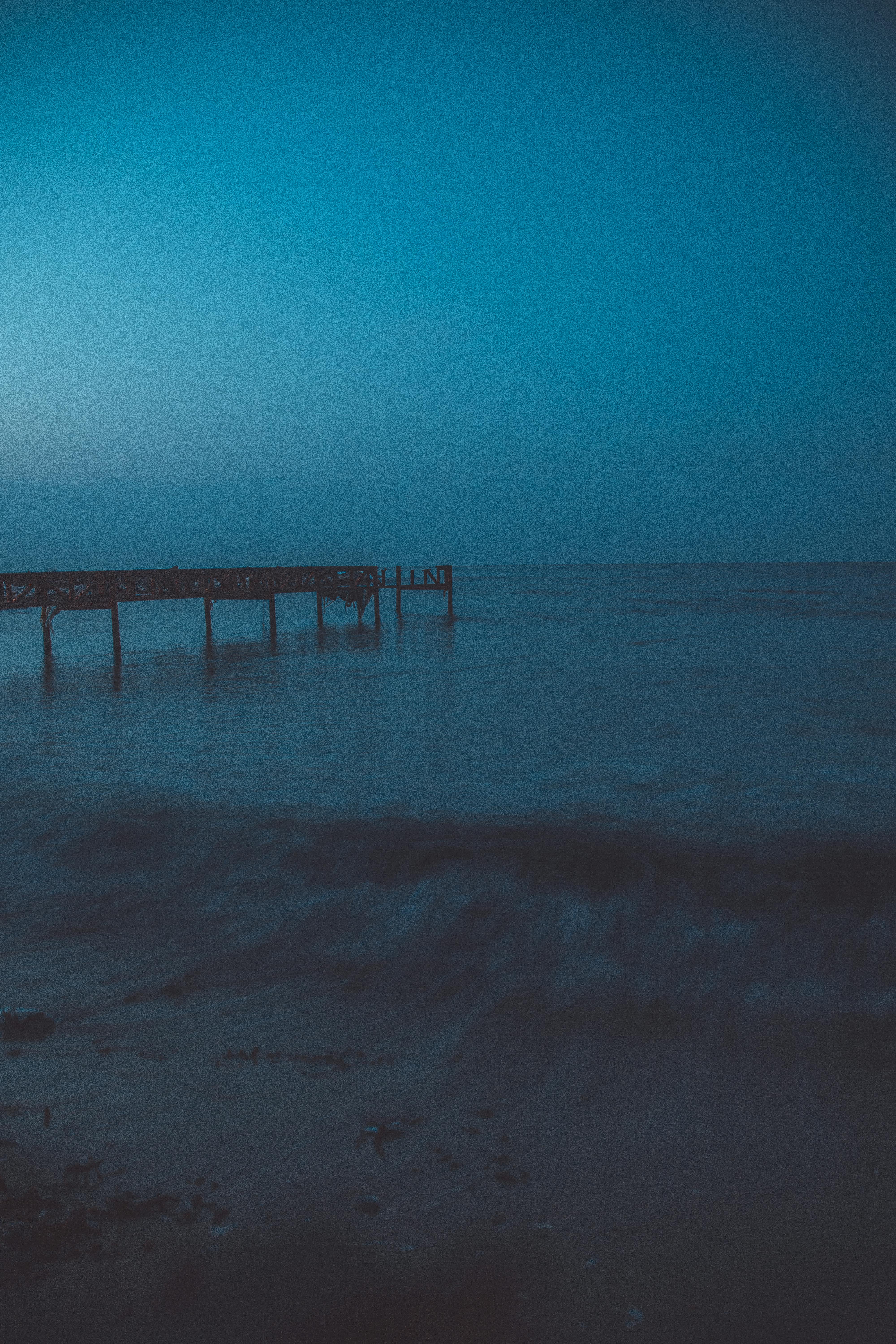 A tranquil view of the ocean with a pier at dusk in Cyprus, featuring calm waves and a clear horizon.