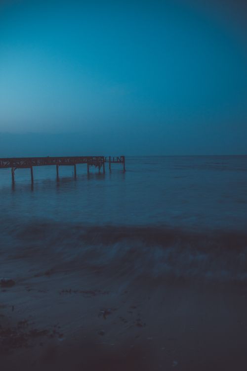 Free A tranquil view of the ocean with a pier at dusk in Cyprus, featuring calm waves and a clear horizon. Stock Photo