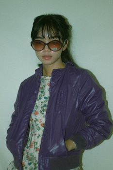 Fashionable woman wearing a purple jacket and sunglasses with floral dress on a white background.