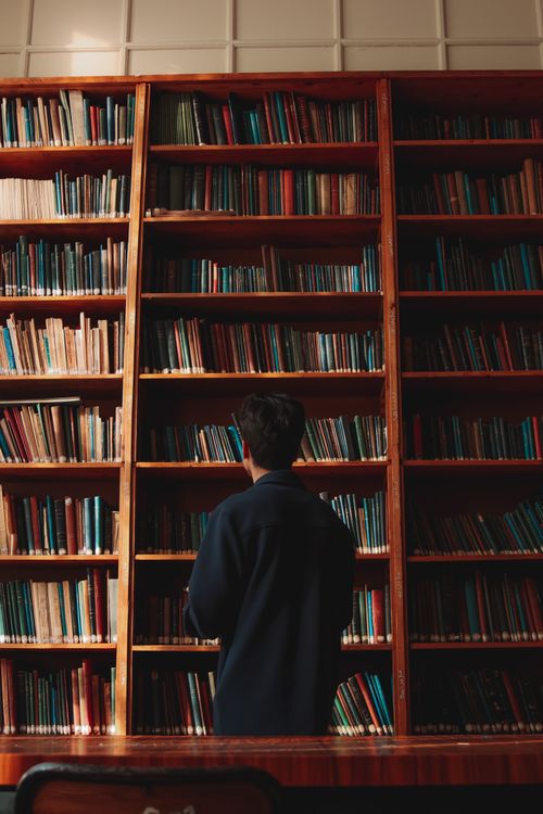 Free A man with short black hair stands in front of bookshelves in a quiet library. Stock Photo
