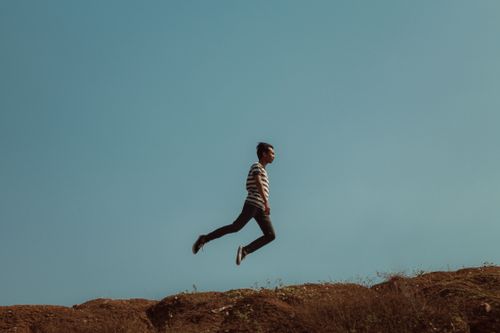 Free A man leaps across a hilltop under a clear blue sky, symbolizing freedom. Stock Photo