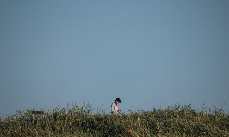 A lone person walks through a grassy field on a sunny day, with ample blue sky.