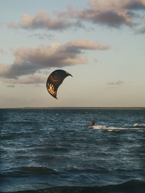 Free A kitesurfer rides the waves under cloud-filled skies at sea, capturing the thrill of outdoor adventure. Stock Photo