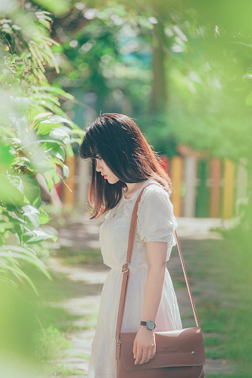 女人穿着白色圆领短袖的衣服站在绿叶植物旁边