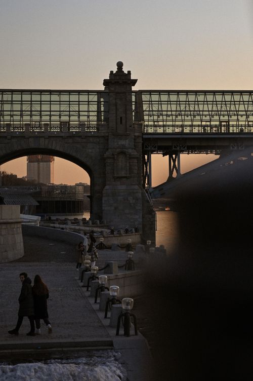 Free A stunning cityscape featuring an urban bridge with people walking, captured at sunset by the river. Stock Photo