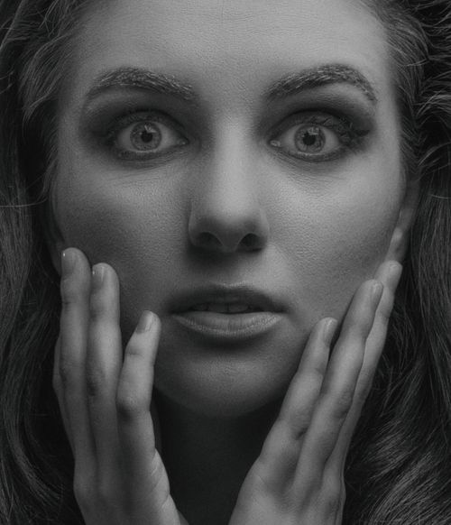 Free Close-up monochrome portrait of a woman with a surprised expression, hands on face. Stock Photo