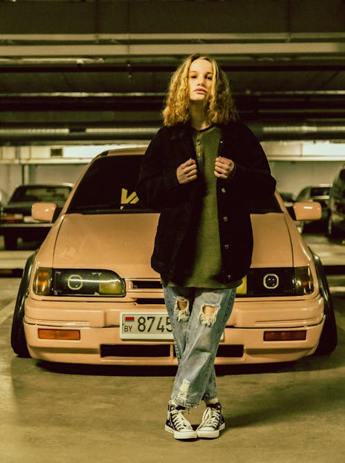 A Woman in Black Jacket and Ripped Jeans Standing Beside the Car